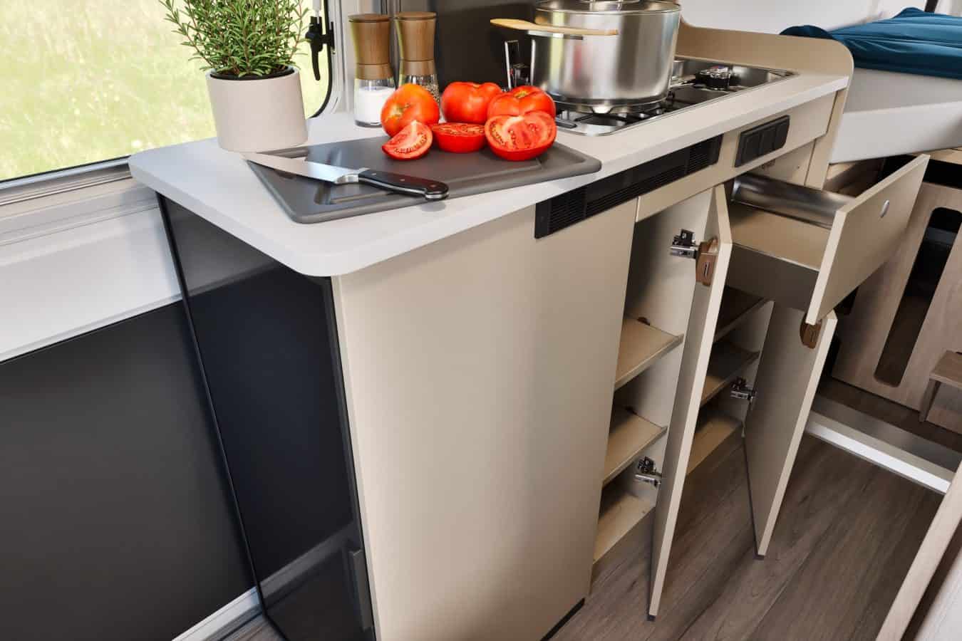 Moderne buscamper keuken met opbergkast, gaskookplaat en verse ingredienten.